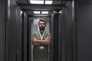 portrait d'un technicien masculin ou d'un administrateur réseau debout courageux comme un héros avec les bras croisés dans la salle des serveurs du centre de données. photo