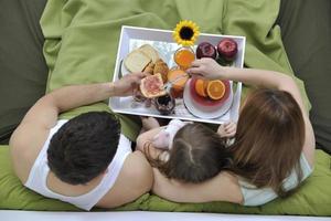 jeune famille heureuse prend son petit déjeuner au lit photo