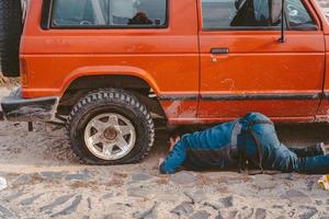 l'homme se trouve sous une voiture 4x4 sur un chemin de terre photo