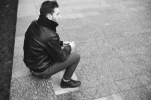 un homme vêtu d'un jean et d'une veste noire s'assoit sur une dalle photo