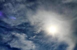 belle vue sur les rayons du soleil avec quelques reflets et nuages dans un ciel bleu photo