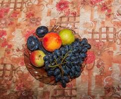raisins, pommes, pêches et prunes dans une assiette sur la table. photo
