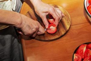 une femme prépare du jus frais et sain à partir de tomates. les mains féminines coupent les légumes sur une planche de cuisine en bois. concept de régime pour un mode de vie sain. photo