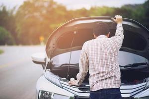 un jeune homme stressé ayant des problèmes avec son accident de salle des machines de voiture cassée par le stress à un moteur en panne attend de l'aide. photo