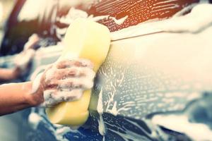personnes travailleur homme tenant la main éponge jaune et fenêtre nettoyante en mousse à bulles pour laver la voiture. concept de lavage de voiture propre. laisser de la place pour écrire des messages.