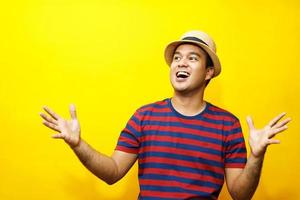 portrait de hipster jeune homme jeune homme heureux tenue décontractée t-shirt rayé rouge et porter un chapeau. geste émotion étendre les bras timide modeste sur les portraits de studio mis en couleur fond jaune. photo