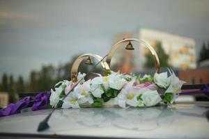 anneaux de mariage sur le toit de la voiture. des fleurs blanches et des cloches ornent la voiture des jeunes mariés. photo