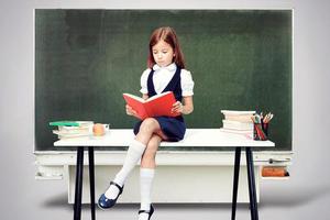 jeune fille mignonne assise à la table et lisant un livre photo