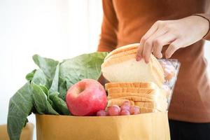 belle main femme attrape le pain du sac en papier brun. Commandez à l'épicerie en ligne pour une livraison à domicile. photo