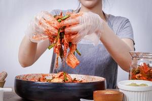 femme asiatique assise et faisant du kimchi, elle porte des gants de protection et un chapeau. pour garder les aliments propres. fond blanc concept de nourriture fermentée coréenne à base de légumes. photo