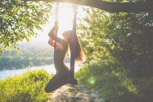 une jeune gymnaste féminine est engagée dans le yoga aérien, en utilisant une combinaison de poses de yoga traditionnelles, de pilates et de danse en utilisant un hamac au coucher du soleil dans la nature. mode de vie sain.