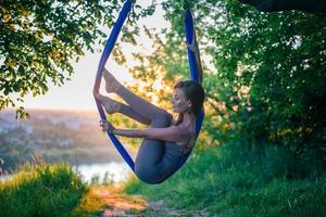 un jeune gymnaste est engagé dans le yoga aérien dans la nature dans le parc, en utilisant une combinaison de poses de yoga traditionnelles, de pilates et de danse douce photo