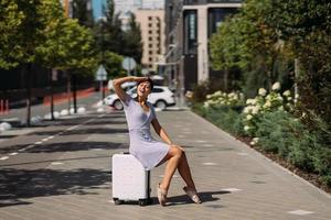 jolie jeune femme est assise sur une valise à l'extérieur. photo