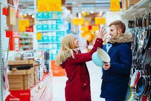 le gars et la fille choisissent une marmite et une poêle à frire dans un supermarché. photo