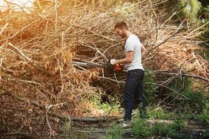 l'homme aux bottes authentiques et aux jeans selvedge avec une tronçonneuse sur fond de branches photo