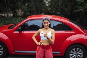 portrait d'une jolie femme caucasienne debout contre une nouvelle voiture rouge photo