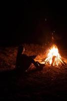 femme assise et se réchauffer près du feu de joie dans la forêt nocturne. photo