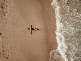 vue aérienne de dessus jeune femme allongée sur la plage de sable et les vagues photo