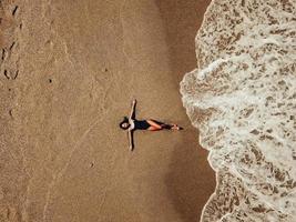vue aérienne de dessus jeune femme allongée sur la plage de sable et les vagues photo