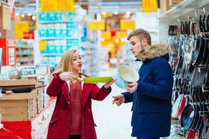 le gars et la fille choisissent une marmite et une poêle à frire dans un supermarché. photo