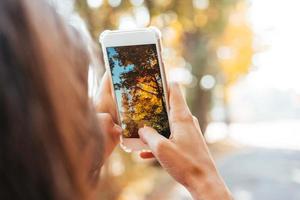 femme prend une photo d'un arbre d'automne dans une rue