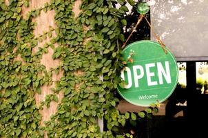 Panneau vert suspendu avec message ouvert sur la fenêtre avec des feuilles de lierre sur un mur en bois au café photo