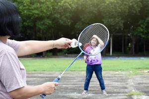 jeu de badminton en plein air, mise au point douce et sélective sur le volant blanc, arrière-plan flou de la femme asiatique et des arbres, concept de jeu de badminton en plein air pendant les temps libres et l'activité quotidienne. photo