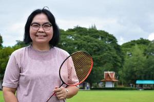 jeu de badminton en plein air, mise au point douce et sélective sur le volant blanc, arrière-plan flou de la femme asiatique et des arbres, concept de jeu de badminton en plein air pendant les temps libres et l'activité quotidienne. photo