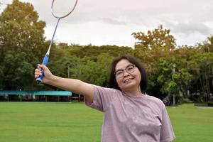 jeu de badminton en plein air, mise au point douce et sélective sur le volant blanc, arrière-plan flou de la femme asiatique et des arbres, concept de jeu de badminton en plein air pendant les temps libres et l'activité quotidienne. photo