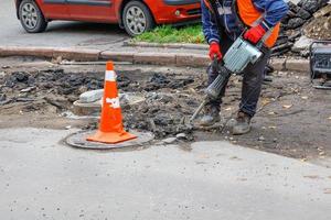 un travailleur à l'aide d'un marteau-piqueur électrique et d'un générateur à essence nettoie la zone près des regards d'égout de l'ancien asphalte. photo