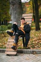 jeune homme assis sur un banc dans le parc et écoutant de la musique photo