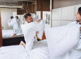 un couple joyeux s'amuse dans la chambre à se battre avec de gros oreillers à la maison photo