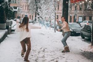 un jeune couple joyeux joue aux boules de neige dans la rue. photo