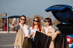 jeunes femmes à la voiture avec des sacs à provisions. les filles prennent un selfie photo