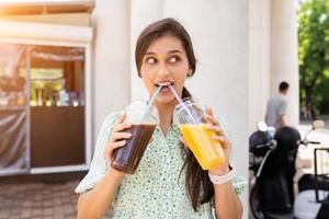 jeune femme boit deux cocktails avec de la glace dans des gobelets en plastique avec de la paille photo