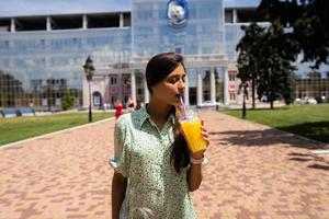 jeune femme souriante et buvant un cocktail avec de la glace dans une tasse en plastique avec de la paille photo