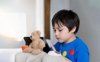 écolier utilisant une tablette pour ses devoirs, enfant regardant une tablette numérique avec un visage pensant, jeune garçon regardant un dessin animé sur un pavé tactile, nouveau style de vie normal avec apprentissage en ligne, concept d'apprentissage à domicile photo