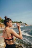femme buvant de l'eau fraîche de la bouteille après l'exercice sur la plage photo