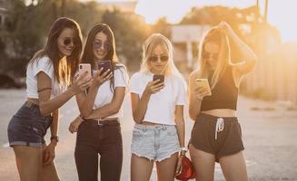 quatre jolies femmes se tiennent sur un parking avec des smartphones photo