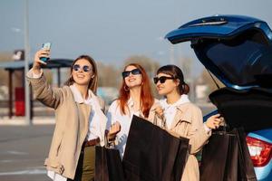 jeunes femmes à la voiture avec des sacs à provisions. les filles prennent un selfie photo