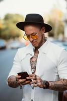 un jeune homme avec un chapeau et des lunettes de soleil tient un téléphone portable dans ses mains photo