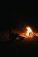 femme assise et se réchauffer près du feu de joie dans la forêt nocturne. photo