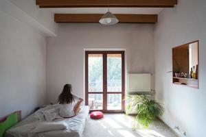 jeune femme assise sur le lit et regardant par la fenêtre. photo