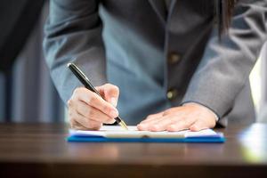 lieu de travail gros plan personne femme d'affaires professionnelle assise au bureau tenir la signature du stylo ou le papier du contrat de signature. femme employée écrit un document d'accord sur le formulaire de paperasse d'entreprise au bureau de travail photo