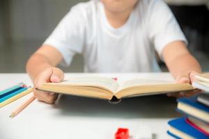 un garçon assis étudie à l'intérieur à la maison, un étudiant en ligne apprend et fait ses devoirs sur le bureau, un jeune enfant lit et écrit un livre sur la table. concept d'éducation, cyberespace technologique photo