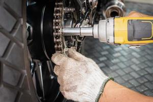 mécanicien de moto portant des gants à l'aide d'une clé à chocs et d'une douille d'entraînement réparant le pignon arrière de la moto au garage de motos, concept d'entretien et de réparation de motos, photo