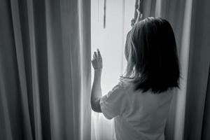 vue arrière d'une femme tenant un rideau et regardant par la chambre. femme déprimée et stressée. concept de journée mondiale de la santé mentale. sensibilisation à la santé mentale. femme réfléchie dans une pièce sombre. femme malheureuse. photo