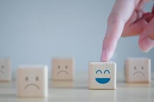 point de main vers un visage heureux parmi des visages malheureux sur des blocs de bois. pensée positive, rétroaction, satisfaction, examen du service client, évaluation de la santé mentale, concept de la journée mondiale de la santé mentale. photo