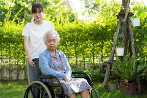 soignant aide et soins asiatique senior ou âgée vieille dame patiente assise sur un fauteuil roulant dans le parc, concept médical fort et sain. photo