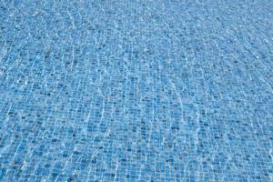 le vent fait onduler l'eau. arrière-plan abstrait de l'eau de surface claire. piscine bleue reflétant le soleil ridée. motif du fond de la piscine en carreaux bleus en céramique mosaïque ondulée. photo